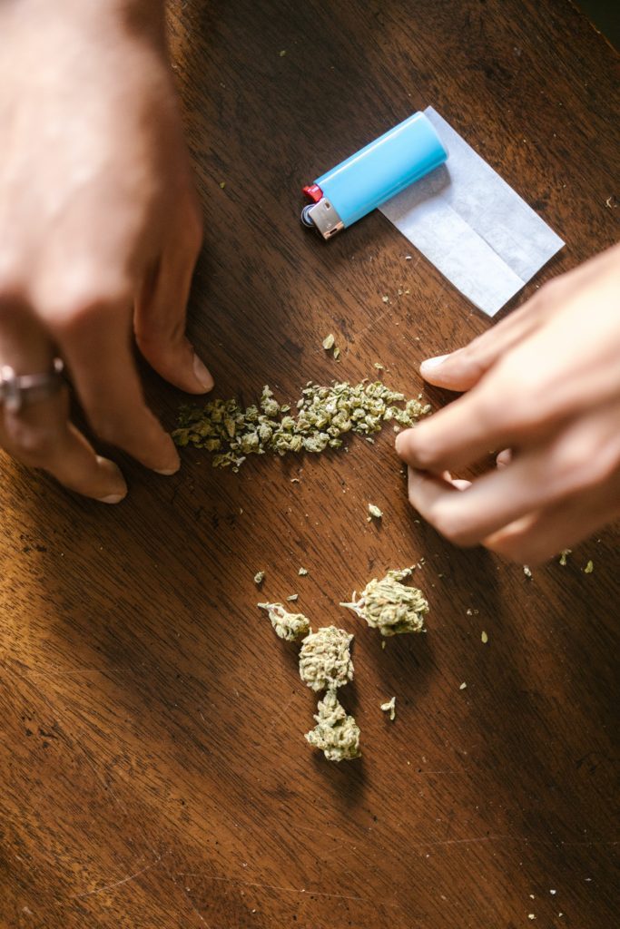 Photo of marijuana buds on a brown table, with hands breaking it up and rolling into a joint